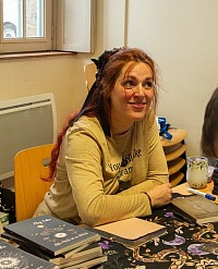 Elsy Eala, autrice de romans fantastiques, en séance de dédicace avec ses ouvrages, derrière une table ornée d’illustrations occultes.